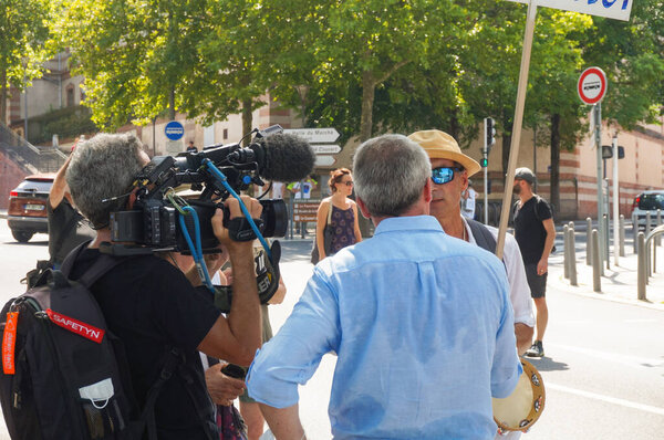 Albi, France - Aug. 14, 2021 - A sweaty journalist in blue shirt of the State-owned TV channel France 3 interviews an opponent to mandatory vaccination for health workers and sanitary passport