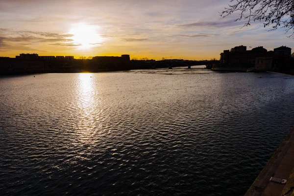 Yüzeyde dalgalar ve suda gün batımının yansımasının yer aldığı Garonne Nehri üzerindeki akşam manzarası Fransa 'nın Toulouse kentindeki Saint-Cyprien semtindeki binaların siluetleri