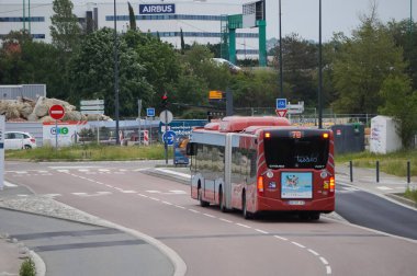 Toulouse, Fransa - 10 Haziran 2023 - Ulaştırma şirketi Tisso tarafından işletilen kırmızı, eklemli bir belediye otobüsü Montaudran Yenilik Kampüsü tarafından Labge 'deki Airbus Savunma ve Uzay Fabrikası' na doğru sürüyor.