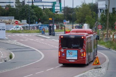 Toulouse, Fransa - 10 Haziran 2023 - Ulaştırma şirketi Tisso tarafından işletilen kırmızı, eklemli bir belediye otobüsü Montaudran Yenilik Kampüsü tarafından Labge 'deki Airbus Savunma ve Uzay Fabrikası' na doğru sürüyor.