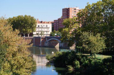 Toulouse, Fransa - 7 Ekim 2023 - Ramier Adası 'nda yeşil manzara, Saint-Michel' de tuğladan apartmanlar, Garonne Nehri 'ni geçen Pont de Halage de Tounis adında kemerli bir köprü