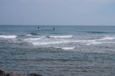 Port-la-Nouvelle, Fransa - 5 Nisan 2024 - Akdeniz kıyısındaki sahil tatil beldesi açıklarında, Narbonne bölgesinde; uzaklarda, tam teçhizatlı dalgıç kıyafetleri giymiş iki tatilci, folyo levhalarıyla dalgalarda sörf yapıyor.