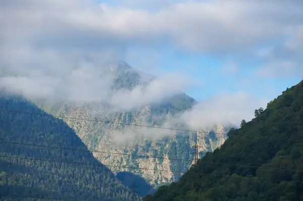 stock image Vielle-Aure - July 25, 2024 - A rock mass in Saint-Lary-Soulan ski resort in summer, in the French Pyrenees Mountains, covered with pine forest, is topped and partially hidden by the morning clouds