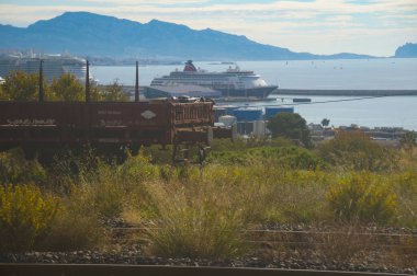 Marseille, France - Oct. 20, 2024 - In the forefront, an abandoned freight train; in the background, in the blur, cruise ships in the passenger terminal of the commercial port of Marseille, PACA clipart