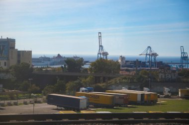 Marsilya, Fransa - 20 Ekim 2024 - Marsilya ticari limanında yarı karavan kamyonları olan bir Dachser lojistik merkezi; arka planda yolcu gemileri, iskele vincleri ve konteyner gemileri