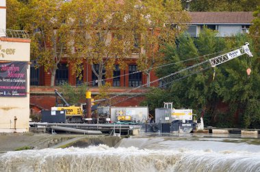 Toulouse, France - Oct. 19, 2024. Crawler crane on a platform floating on the Garonne River, operated by Buesa TMF for EDF for maintenance hydraulic works on the weir and hydropower plant of Bazacle  clipart