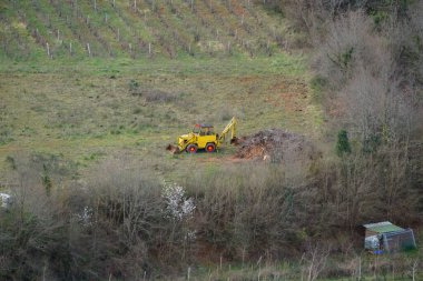 Coustaussa, Fransa - 29 Mart 2025 - Aude Vadisi 'ndeki Corbires Dağları' nın yamacındaki bir üzüm bağının altında, tarımın ortasındaki eski sarı bir kepçe üzerinde hava manzarası