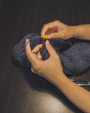 İki el sarı bir kanca iğnesi ve örgü ipliği tutuyor. Örgü örme sürecini gösteriyor..