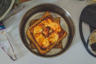 Lezzetli bir ev yapımı tost pizzası, kilerdeki zımbalarla yapılabilecek hızlı ve kolay bir yemek. Tabakta erimiş peynirle kaplı ekmek dilimleri yer alıyor..