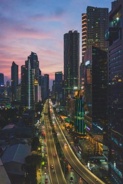 Jakarta, Endonezya - 12 Mayıs 2024. Bu fotoğraf Jakarta 'nın dinamik şehir manzarasını alacakaranlıkta yakalar. Modern gökdelenler gökyüzüne uzanır, pencereleri parlak bir şekilde parlar. Trafik yükseltilmiş otoyol boyunca ışık şeridi gibi akar..