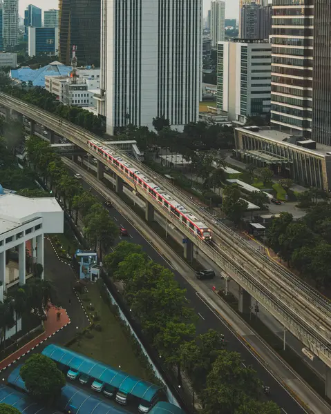 stock image Jakarta, Indonesia - May 12th, 2024.  a city in constant motion. A red train streaks through the urban landscape, a symbol of the city's progress and development.  Below, the downtown LRT system winds its way through the dense clusters of skyscrapers