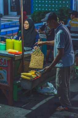 Balikpapan, Endonezya - 15 Haziran 2024 Müşterileri için mısır kızartan bir sokak yemeği satıcısı..