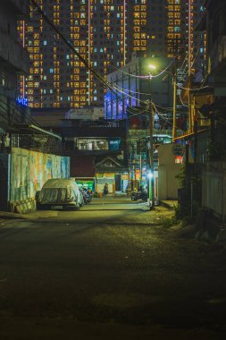 Balikpapan, Endonezya - 3 Eylül 2024, bir şehrin dar bir sokağı. Sokak lambalarıyla aydınlatılmış. Caddenin kenarına park etmiş arabalar ve elektrik hatları var..