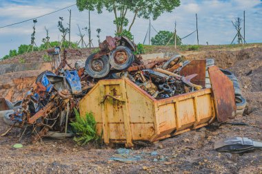 Çöpe atılmış makineler ve hurda metallerle dolu paslı metal bir kap. Görüntü endüstriyel atıkların çevresel etkilerini vurguluyor.