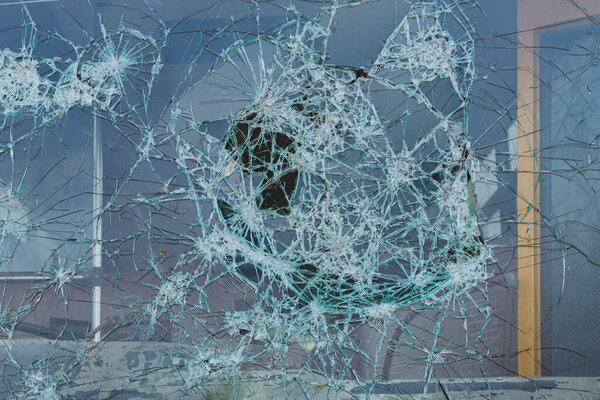 Разбитое окно с большим отверстием и зубчатыми краями, показывающее разрушительную силу удара.