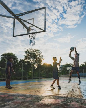 Balikpapan, Endonezya - 12 Kasım 2024. Gençlerden oluşan bir grup arkadaşça bir oyun oynarken güneş basketbol sahasının üzerinde batıyor..
