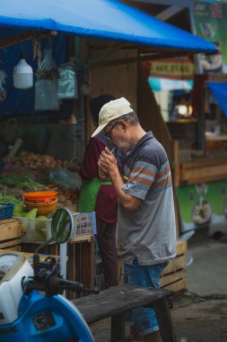 Balikpapan, Endonezya - 25 Aralık 2024. Şapkalı ve gözlüklü yaşlı adam markette sigara yakıyor..