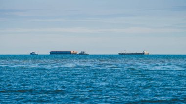 Okyanusta üç gemi, iki römorkör tarafından çekilen merkezi bir mavna, ve daha büyük bir gemi. Sakin denizler ve berrak gökyüzü rutin bir ulaşım operasyonu olduğunu gösteriyor..