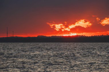 Balikpapan Körfezi 'nde çarpıcı bir günbatımı. Koyu kırmızı bir gökyüzü. Karanlık ufukta parlayan bulutlar..