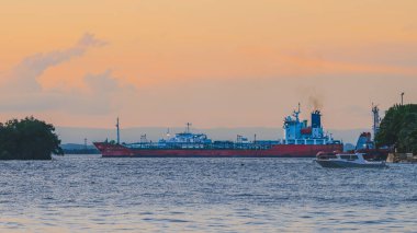 Balikpapan, Endonezya - 31 Mart 2025. Alacakaranlıkta Balikpapan Körfezi 'nde küçük bir teknesi olan büyük bir tanker gemisi demirledi. Yumuşak, pastel gökyüzü ve sakin su sakin ama endüstriyel bir manzara yaratır..