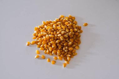 Kısa açıklama: Pürüzsüz, soluk gri bir yüzeye dağılmış küçük bir yığın sarı, kurutulmuş patlamış mısır tanelerinin yakın çekimi.