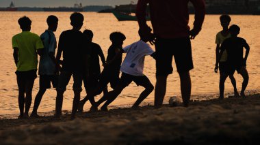 Gün batımında plajda yalınayak futbol oynayan bir grup genç, altın deniz altının gölgesinde yakalandı..