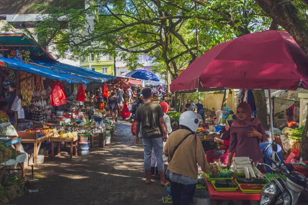 Balikpapan, Endonezya - 19 Nisan 2025. Yerel halk, sıcak bir sabahta ağaçlar ve renkli şemsiyelerle gölgelenmiş Pandan Sari pazarında alışveriş ve satış yapıyor..