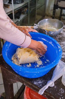 Bir fırın mutfağında ekmek hazırlarken mavi bir kasede hamur yoğuran ellerin yakın çekimi..