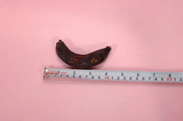 rotten Banana and tape measure on pink Background, copy space. rotten bananas with measuring tape, upsize penis concept.