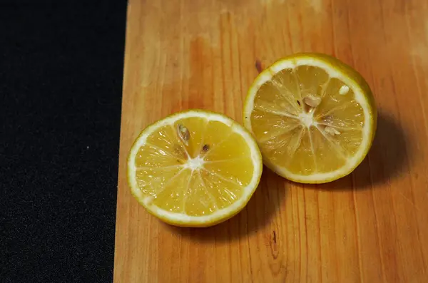 Siyah arka planda ahşap bir altlık üzerinde taze limon dilimleri. Limonlu bir kesim tahtasının yakın plan fotoğrafı.