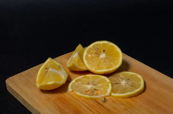 Siyah arka planda ahşap bir altlık üzerinde taze limon dilimleri. Limonlu bir kesim tahtasının yakın plan fotoğrafı.