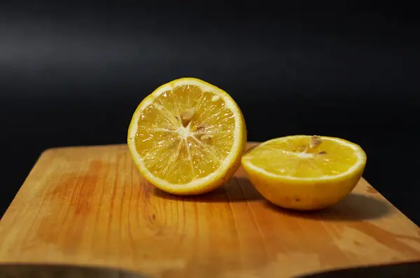 Siyah arka planda ahşap bir altlık üzerinde taze limon dilimleri. Limonlu bir kesim tahtasının yakın plan fotoğrafı.