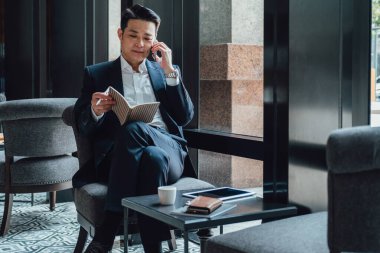 Kahve dükkanında cep telefonuyla konuşan mutlu iş adamı.