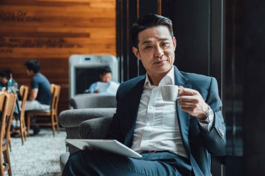 Kahve içen ve dijital tabletini kahve dükkanında tutan mutlu bir iş adamının portresi.