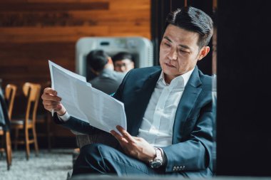 Kahve dükkanında otururken belgeyi analiz eden endişeli bir iş adamı.