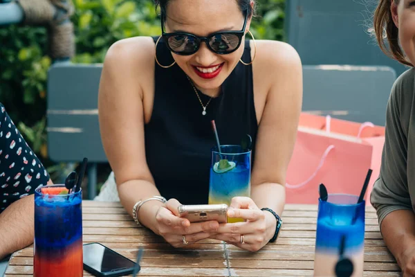 Улыбающаяся Женщина Мобильного Телефона Сидя Кафе Неузнаваемыми Друзьями Выпивая Коктейли — стоковое фото