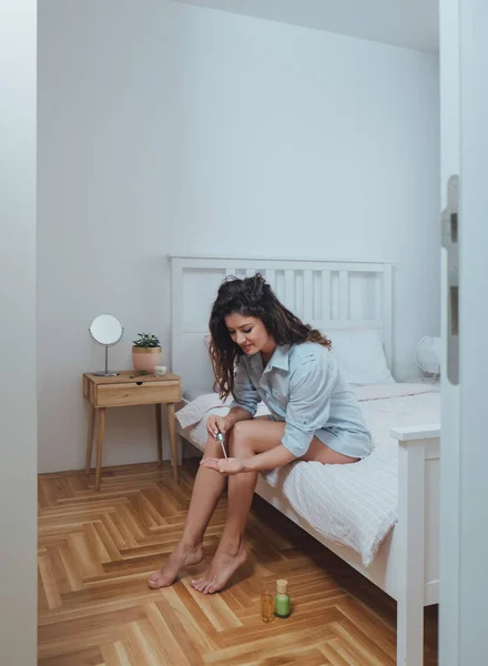 Uśmiechnięta Kobieta Nakładająca Balsam Nogi Sypialni — Zdjęcie stockowe