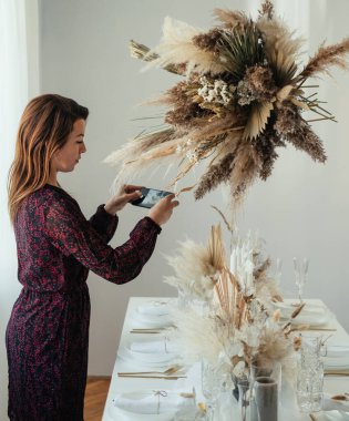 Noel Kutlaması: Ciddi bir kadın evde cep telefonuyla dekore edilmiş yemek masasının fotoğrafını çekiyor