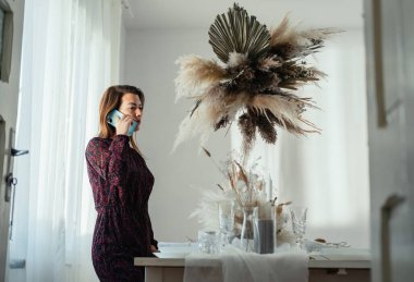 Yılbaşı Hazırlığı: Cep telefonuyla konuşan güzel bir kadın evdeki yemek salonunda sofra kuruyor.