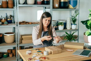 Sıfır atık paketini dükkanında Noel süsleriyle hazırlarken önlüklü kadın makasla ip kesiyor.