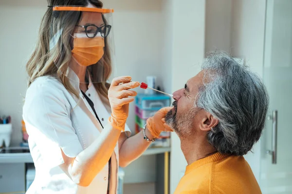 院内の熟女患者から鼻洗浄試験を受ける保護ワークウェアの女医 ロイヤリティフリーのストック写真