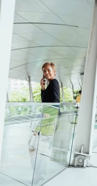 Modern bir terasta cam korkuluklara yaslanırken telefonda konuşan gülümseyen iş kadınının düşük açılı görüntüsü