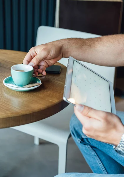 コーヒーを飲みながらコーヒーショップに座っていると 匿名の男がタブレットでビジネスレポートを読んでいるのが見えます ロイヤリティフリーのストック画像