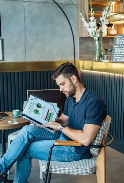 コーヒーと携帯電話のカップでコーヒーショップに座っている間 紙にビジネスレポートを読み グラフを分析 ロイヤリティフリーのストック画像