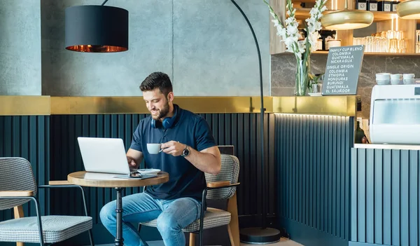 彼のラップトップコンピュータで働く笑顔ビジネスマンとカフェでコーヒーを飲むカップ ストック写真