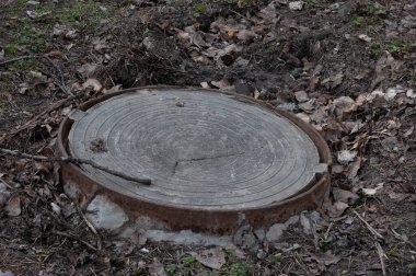 Ormanda paslı bir rögar kapağı var, toprak eski sonbahar yapraklarıyla kaplı..