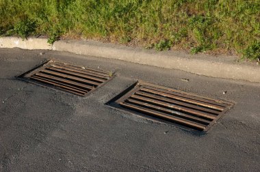 Yeşil çimlerin yanında iki rögar ızgarası.