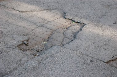 Eski, hasarlı bir yolda asfaltta bir çukur, aşınma ve çürümeyi gösteriyor..