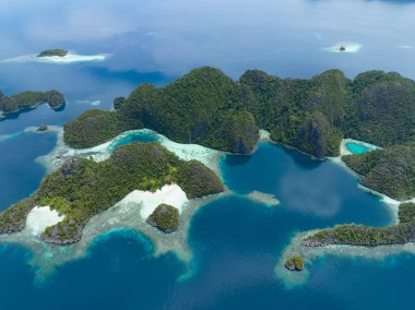 Raja Ampat 'ın deniz manzarasından yükselen dramatik kireçtaşı adalarını çevreleyen güzel mercan resifleri. Endonezya 'nın bu uzak bölgesi inanılmaz deniz biyolojik çeşitliliğiyle bilinir..
