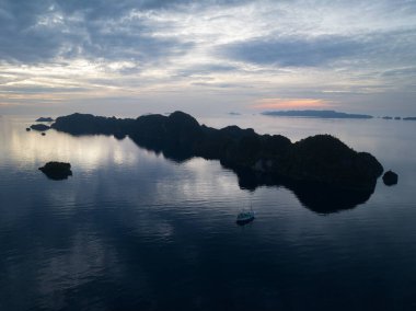 Gün doğumu, Raja Ampat 'ın güzel deniz manzarasından doğan dramatik kireçtaşı adalarını aydınlatır. Endonezya 'nın bu uzak bölgesi inanılmaz deniz biyolojik çeşitliliğiyle bilinir..